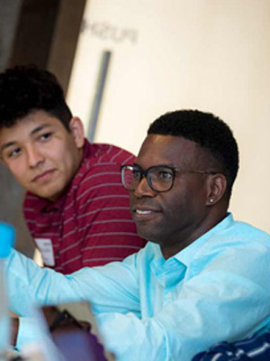 Patrick sitting down at a table and speaking to a group of students