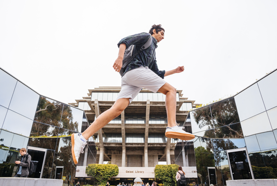 student jumping in front of library