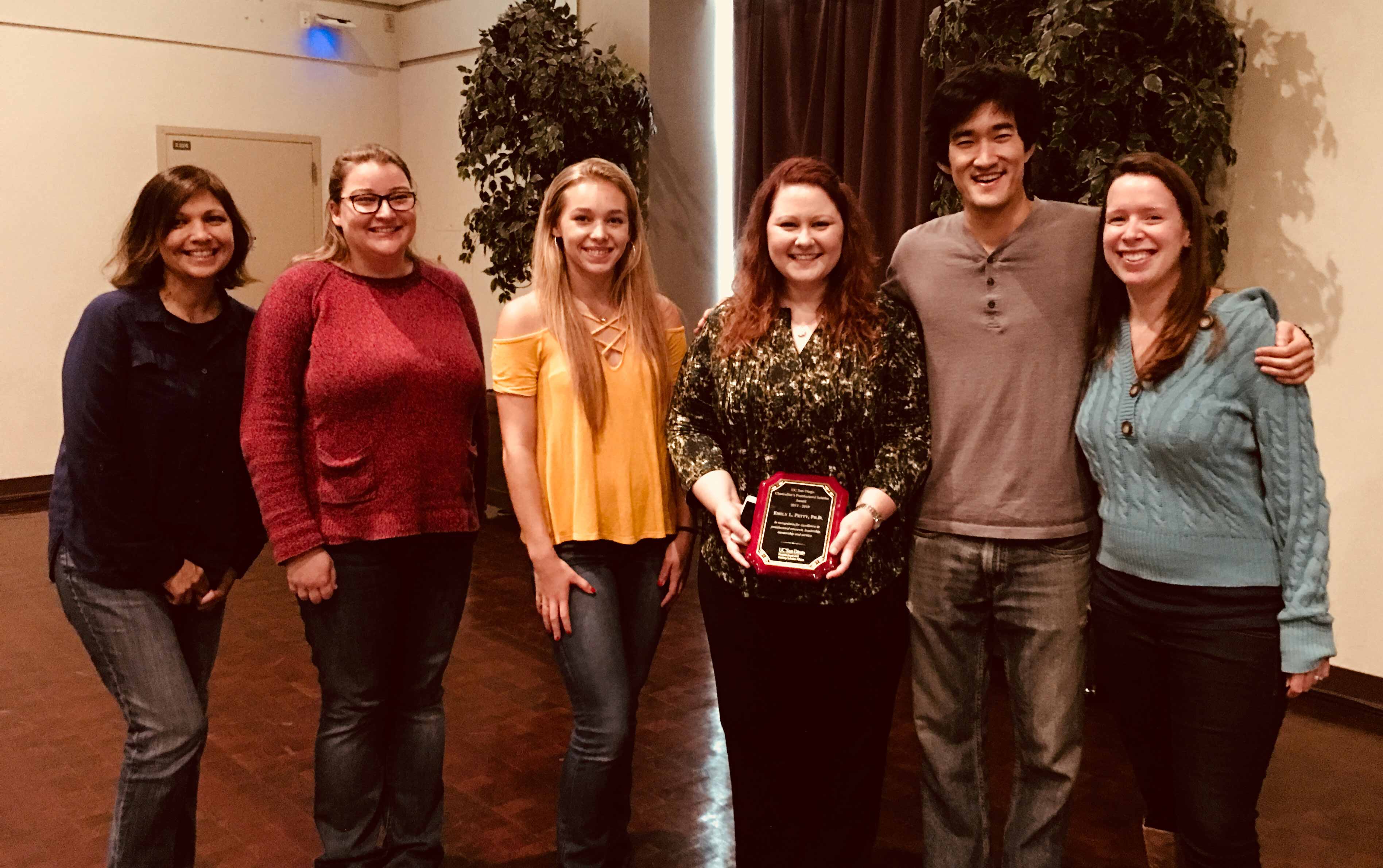 Emily Petty lined up with lab members for a photo with her award plaque